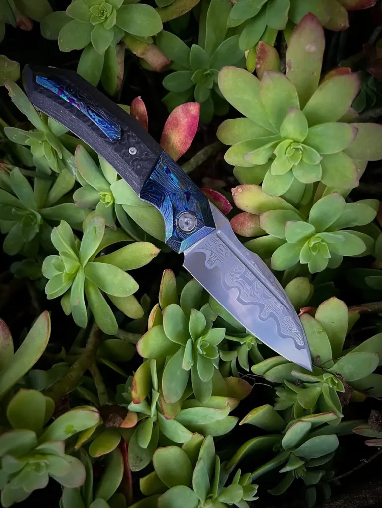 Couteau pliant GTK à lame damas posé dans les plantes